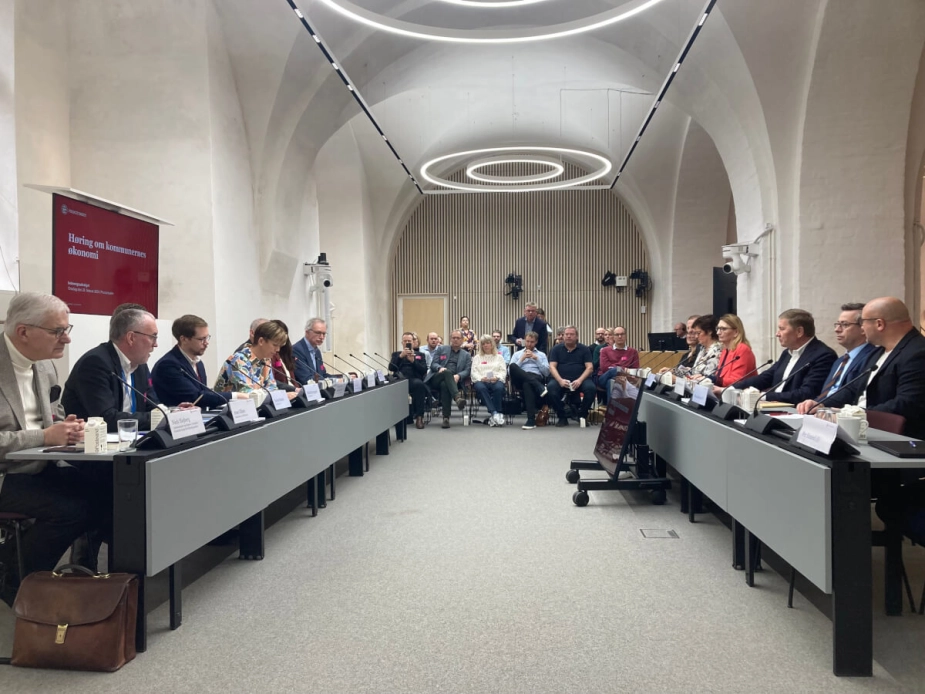 I venstre side af billedet sidder oplægsholderne ved høringen med Theresa Berg Andersen (SF) i midten. På modsatte side sidder folketingspolitikere, hvoraf nogle også er placeret på tilskuerrækkerne. Høringen var velbesøgt, og flere borgmestre fra hele landet var dukket op.